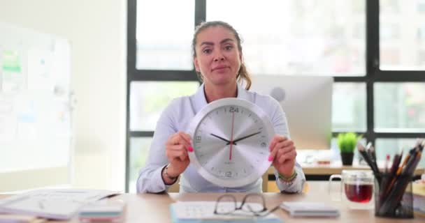 La mujer en la oficina tiene un gran reloj de pared en el lugar de trabajo. Control del tiempo de trabajo - Metraje, vídeo