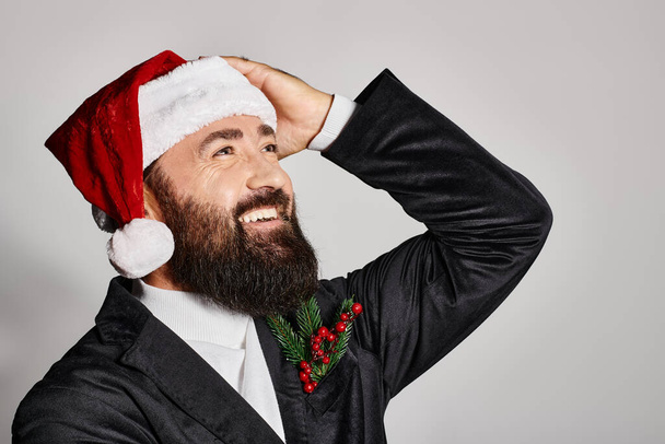 portrait de bel homme barbu en costume élégant et chapeau de Père Noël souriant sur fond gris, Noël - Photo, image