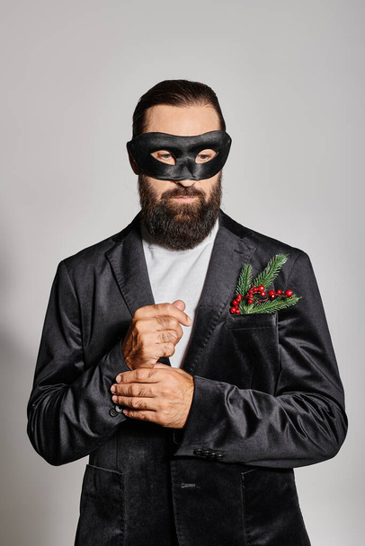 Baile de máscaras de Navidad, hombre barbudo guapo en máscara de carnaval y traje elegante sobre fondo gris - Foto, Imagen