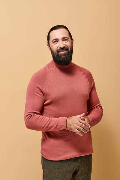 uomo barbuto sorridente in maglione collo alto casual guardando la fotocamera su sfondo beige, moda maschile - Foto, immagini