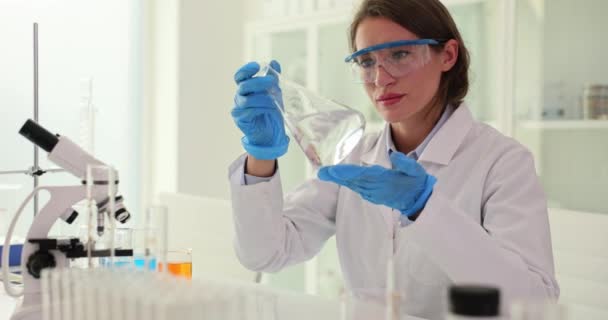 Επιστήμονας συγκρατεί στο χέρι φιάλη με ένα διαφανές υγρό στο εργαστήριο. Δοκιμές ποιότητας νερού - Πλάνα, βίντεο