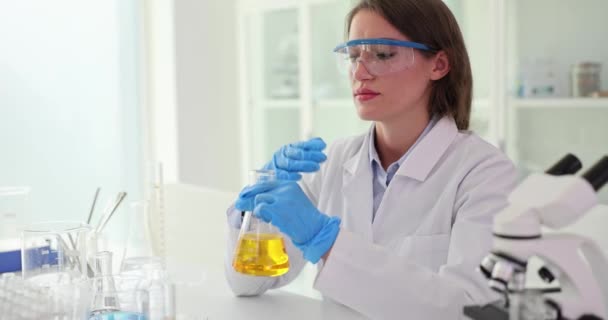 Chemist scientist smells yellow cosmic oil and liquid substance inside glass flask and conducts experiment in laboratory. Scientific research work and aromatherapy research - Footage, Video