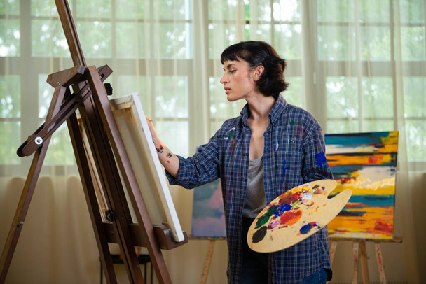 Concentrated woman in front of easel painting at home. - Foto, Imagen