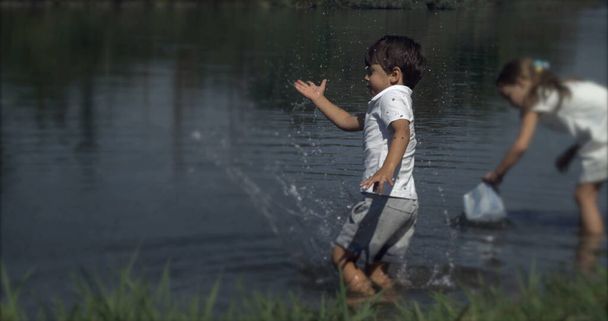 Eau de lac éclaboussant la main de l'enfant dans un mouvement ultra lent. Jeune garçon jouant au bord du lac, collant avec la nature - Photo, image