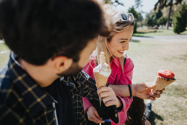 公園で無料の日を過ごしている白人友人,笑い,話し,アイスクリームを食べる. - 写真・画像