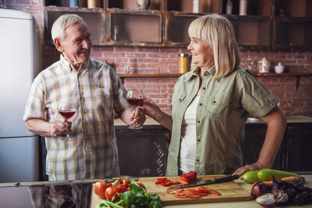 Bella coppia di anziani sta bevendo vino e sorridendo mentre cucinano insieme in cucina
 - Foto, immagini