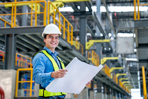 Porträt des professionellen Ingenieurs halten Baudiagramm oder Plan und schauen lächelnd in die Kamera am Arbeitsplatz der Elektro- oder Himmelsbahn. - Foto, Bild
