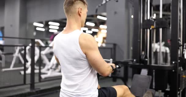 Atletický muž sedící na veslovacím stroji v tělocvičně. Lidé a fitness koncept - Záběry, video