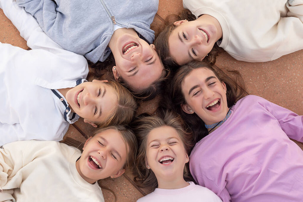 Een groep van zes gelukkige meisjes liggen op hun rug, lachen en genieten. Gelukkige jeugd. Vrienden voor altijd. Foto van bovenaf genomen - Foto, afbeelding