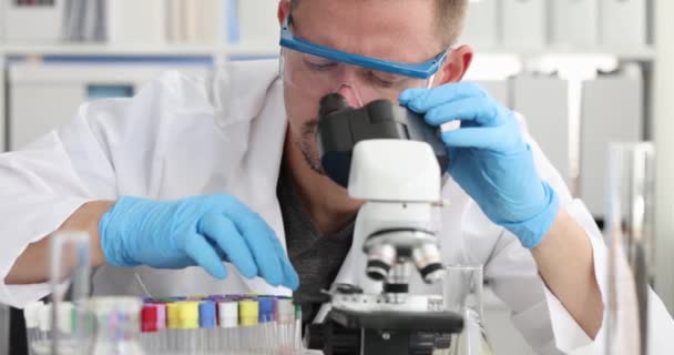 Jovem cientista realiza estudo químico de líquido a partir de tubos de ensaio em microscópio. Conceito de métodos de pesquisa bacterioscópica - Filmagem, Vídeo