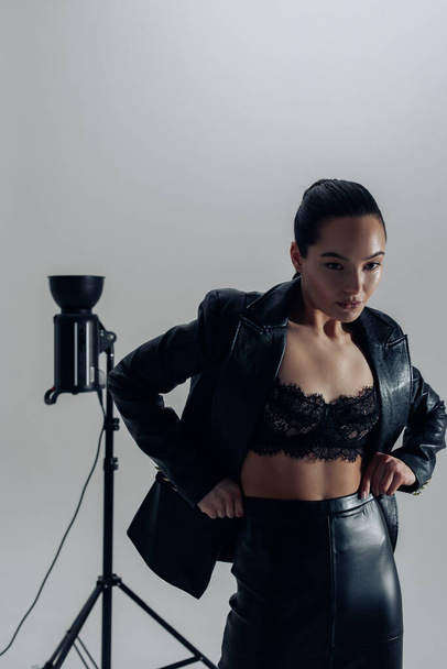 fiatal csinos nő fekete csipke melltartó, bőr szoknya és kabát pózol stúdióban közel fénykép reflektorfény. - Fotó, kép