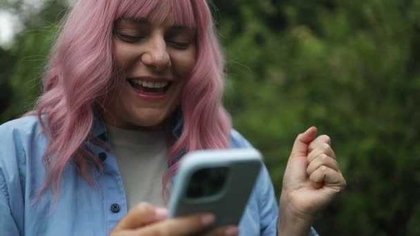 Κοντινό πλάνο της γυναίκας ροζ μαλλιά κρατώντας ένα ψηφιακό smartphone ανάγνωση ένα μήνυμα κειμένου στο τηλέφωνό της, ενώ μεταβαίνει στην εργασία στην πόλη. Υψηλής ποιότητας φωτογραφία - Πλάνα, βίντεο