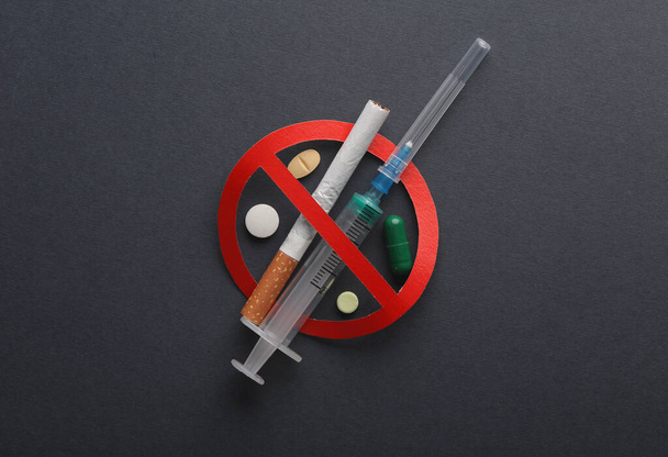 Ας σταματήσουμε τον εθισμό στα ναρκωτικά. Σύριγγα και τσιγάρο, χάπια με ταμπέλα ποτοαπαγόρευσης σε σκούρο φόντο - Φωτογραφία, εικόνα