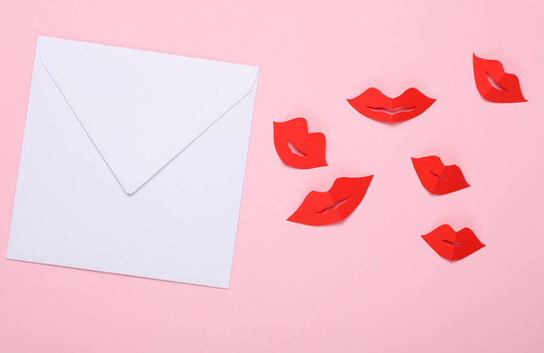 Белый конверт с красными женскими губами, вырезанными из бумаги на розовом фоне. Любовное письмо. День Святого Валентина. Вид сверху - Фото, изображение