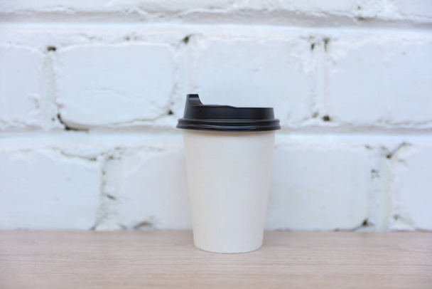 Maqueta de taza de café de cartón blanco sobre fondo de pared de ladrillo blanco - Foto, Imagen