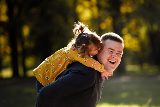 Papá alegre abraza a su pequeña hija sonriente. Papi soltero y el niño se divierten, ríen y disfrutan de la naturaleza al aire libre en el parque de otoño. Concepto de cuidado parental y feliz infancia sin preocupaciones. Feliz día de los padres. - Foto, Imagen