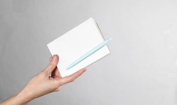 La mano de la mujer sostiene el cuaderno con una cubierta blanca y un bolígrafo sobre fondo gris. Plantilla para diseño - Foto, Imagen