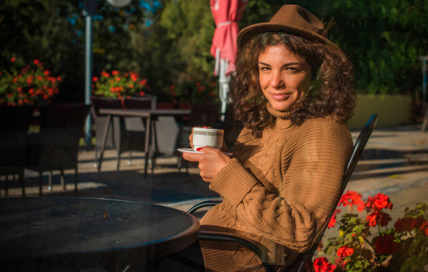 Moderna mujer hispana agradable de mediana edad en suéter de punto con una taza de café en la mañana día soleado relajante - Foto, imagen