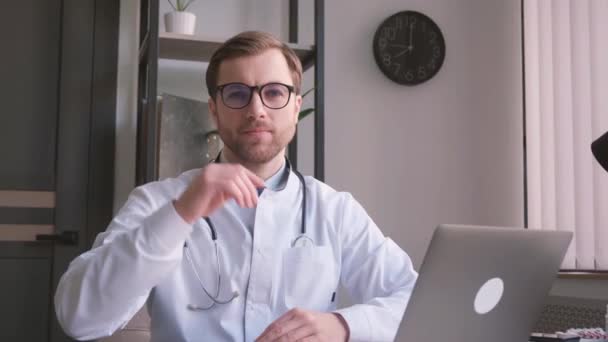 Ein junger Arzt nimmt seine Brille ab und blickt in die Kamera. Arzt bei der Arbeit im Büro. - Filmmaterial, Video