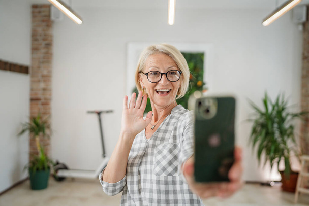 Eine Frau reifen kaukasischen Frau zu Hause oder im Büro mit dem Handy halten Smartphone Selfie-Fotos Selbstporträt oder machen Sie ein Video-Telefonat tägliche Routine Kopierraum - Foto, Bild