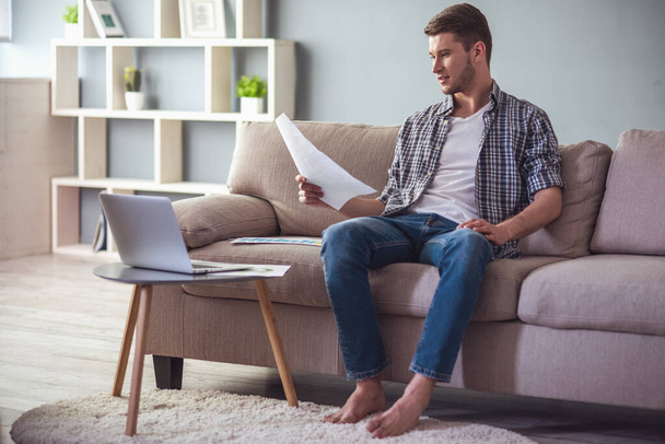 Handsome young businessman in casual clothes is studying documents and smiling while working at home - Photo, Image