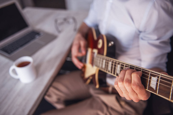 Обрізаний образ молодого бізнесмена, який грає на гітарі в своєму офісі під час перерви
 - Фото, зображення