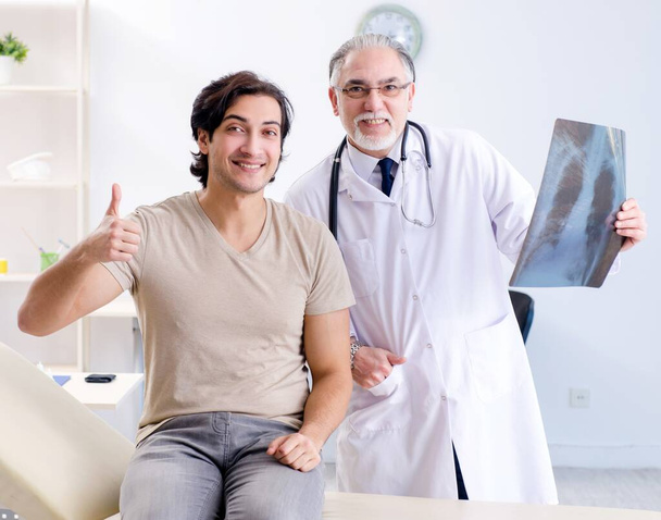De jongeman op bezoek bij oude mannelijke dokter radioloog - Foto, afbeelding