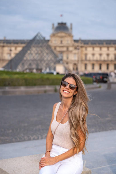 Vertical photo of a smiling tourist sitting next to the entrance of the Louvre museum in Paris - Photo, Image