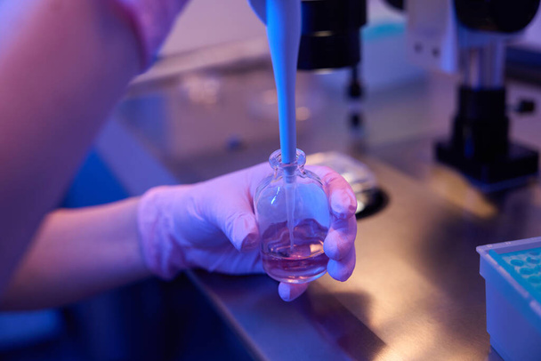 Обрезанное фото ученого в стерильных перчатках, погружающего пластиковый кончик пипетки в бутылку с реагентом - Фото, изображение