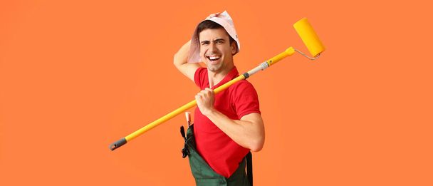 Emotional male decorator with paint roller on orange background - Photo, Image