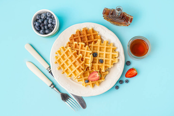 Plate of tasty waffles with berries and maple syrup on blue background - Photo, Image