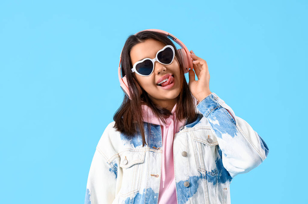 Piękna młoda kobieta w słuchawkach słuchając muzyki na niebieskim tle - Zdjęcie, obraz