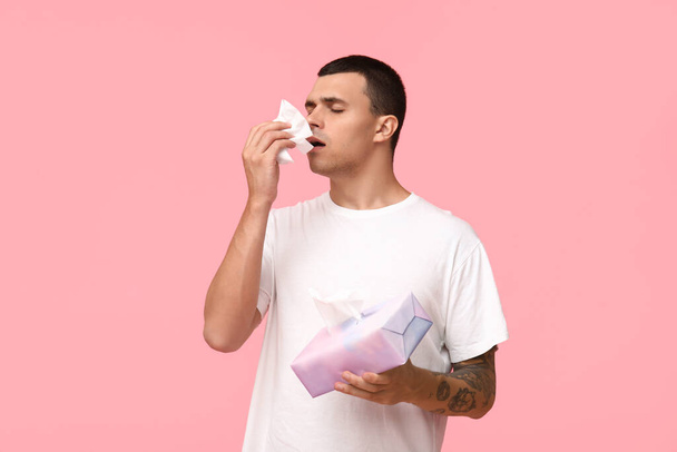 Ill young man with tissues blowing nose on pink background - Φωτογραφία, εικόνα
