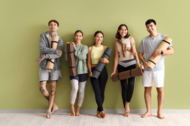 Group of sporty young people with yoga mats near green wall - Photo, Image