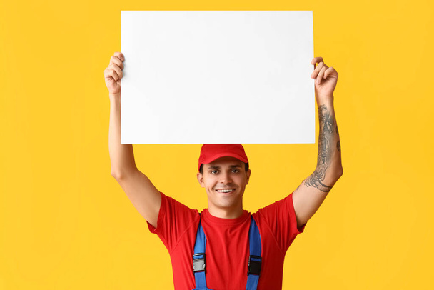 Male car mechanic with blank poster on yellow background - Photo, Image