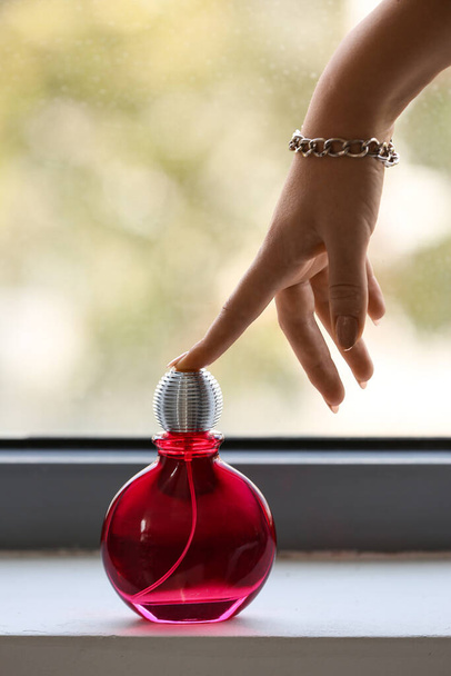 Mão feminina com garrafa de perfume elegante no peitoril da janela em casa - Foto, Imagem
