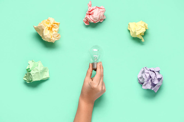 Female hand with crumpled paper and light bulb on green background. Business idea concept - Photo, Image