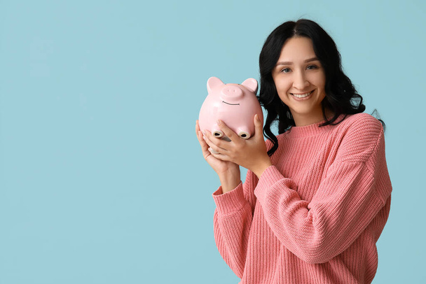 Pretty young woman with piggy bank on blue background - Photo, Image