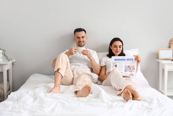 Νεαρό ζευγάρι διαβάζει πρωινή εφημερίδα στην κρεβατοκάμαρα - Φωτογραφία, εικόνα