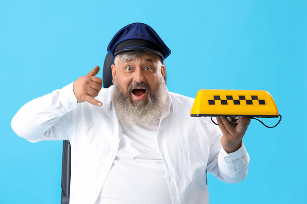 Зрелый шокированный водитель с табличкой на крыше такси, показывающей жест "позвони мне" на синем фоне - Фото, изображение