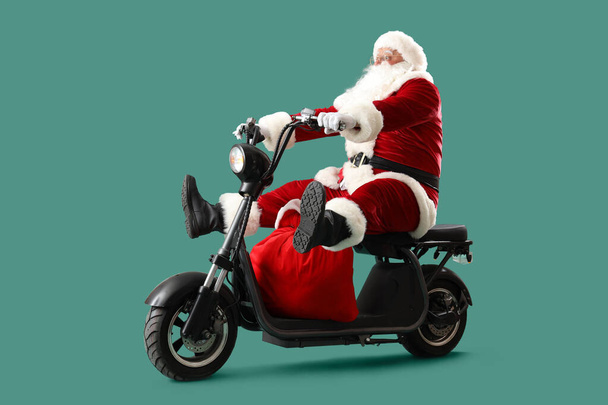 Santa Claus z torbą pełną prezentów świątecznych na skuterze elektrycznym na turkusowym tle - Zdjęcie, obraz