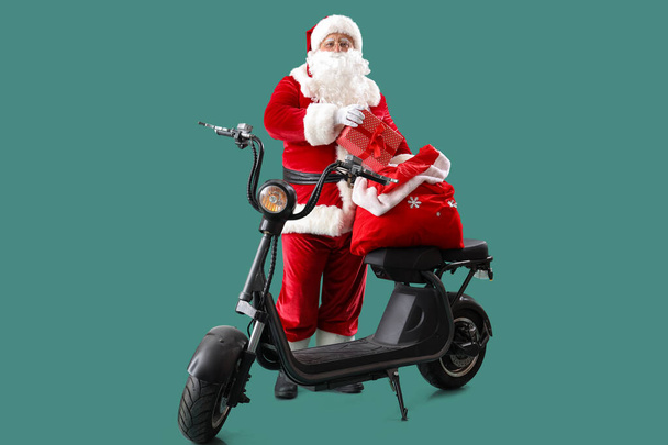 Santa Claus with bag full of Christmas gifts on electric scooter against turquoise background - Photo, Image