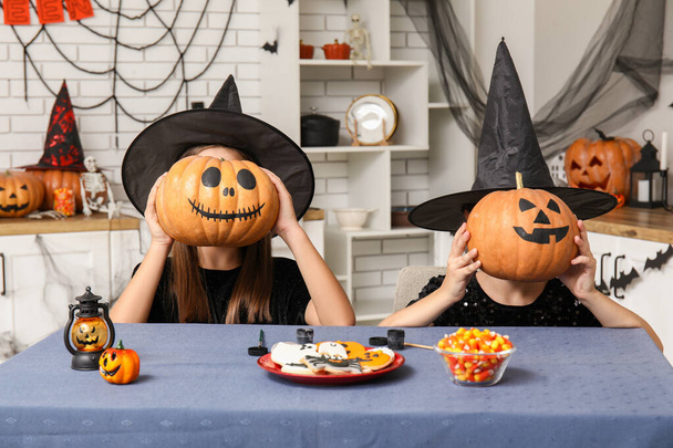 Милые маленькие девочки, одетые на Хэллоуин как ведьмы с конфетами и тыквами за столом на кухне - Фото, изображение