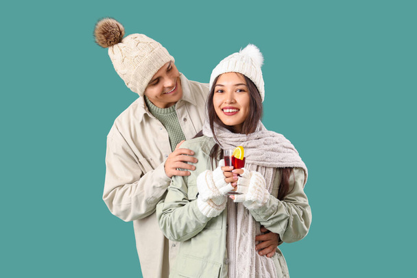Szczęśliwa para w ciepłych ubraniach ze szklanką smacznego grzanego wina na turkusowym tle - Zdjęcie, obraz
