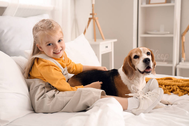 Schattig klein meisje met Beagle hond in slaapkamer - Foto, afbeelding