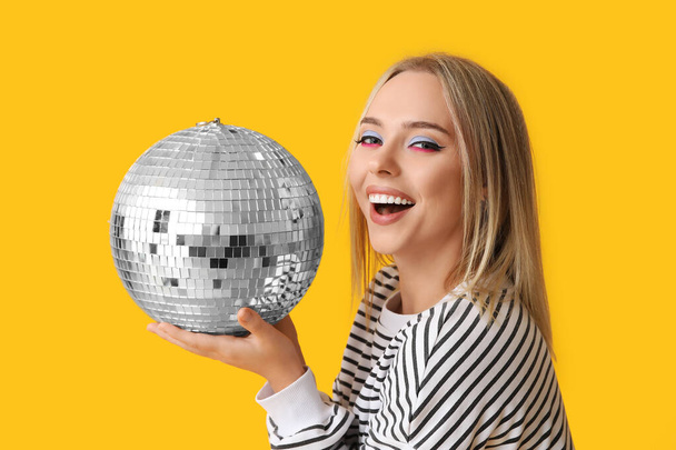Mooie jonge vrouw met discobal op gele achtergrond - Foto, afbeelding
