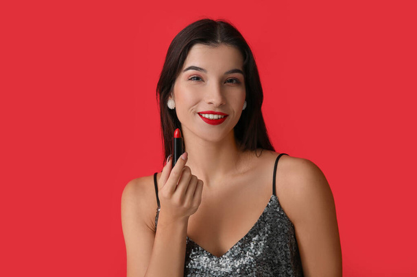 Όμορφη νεαρή γυναίκα με έντονο κραγιόν σε κόκκινο φόντο - Φωτογραφία, εικόνα
