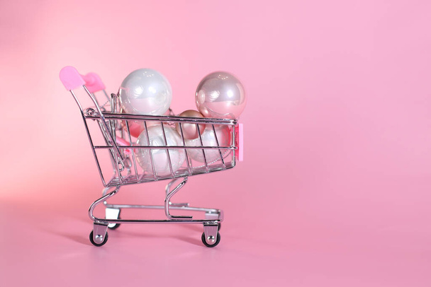 ピンクの背景のクリスマスの装飾の球が付いているショッピング バスケットのトロリー - 写真・画像