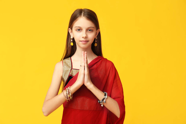 Cute little Indian girl in sari praying on yellow background. Divaly celebration - Photo, Image
