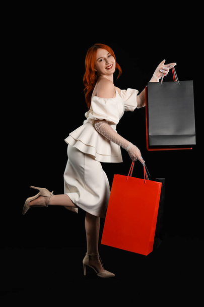 Mooie vrouw en boodschappentassen op donkere achtergrond. Zwarte vrijdag verkoop - Foto, afbeelding